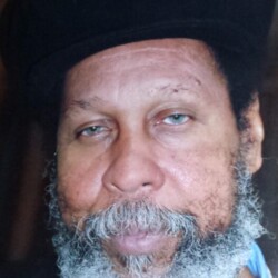 A man with a beard and hat is looking at the camera.